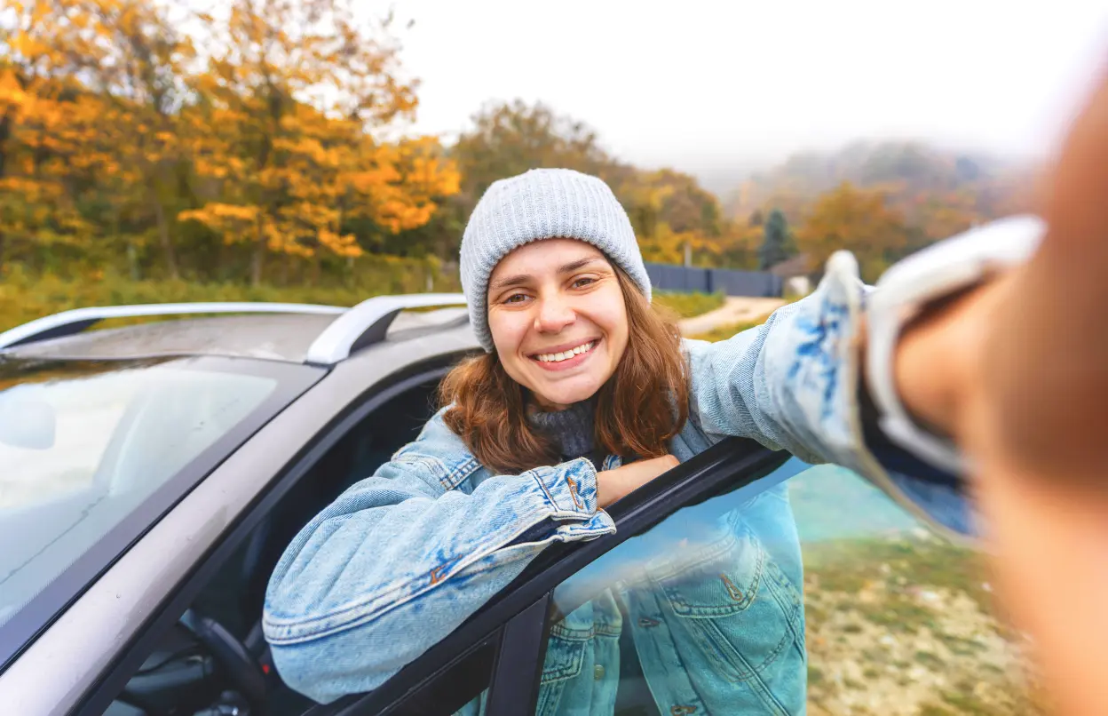 Eine Frau lehnt sich an eine offene Autotür und macht ein Selfie.