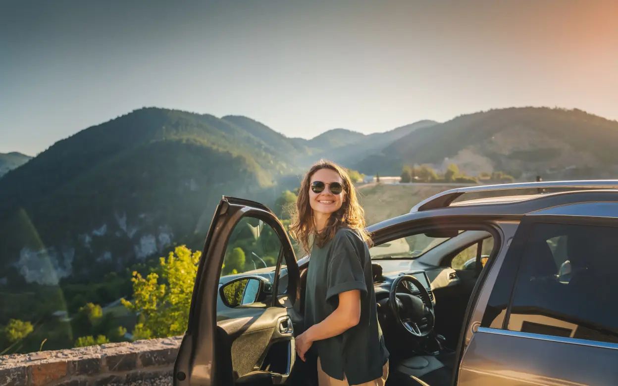 Eine Frau steht an einer geöffneten Autotür und genießt den Ausblick.