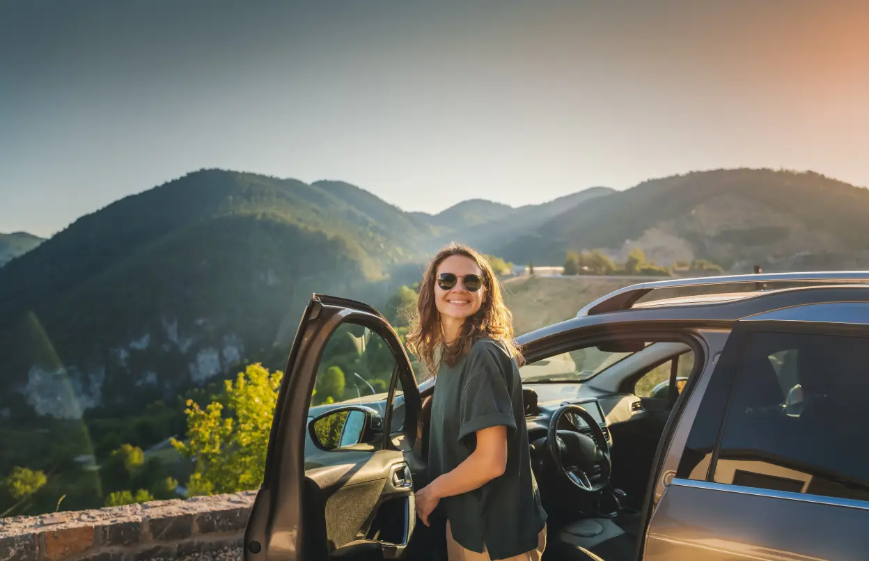 Eine Frau steht an einer geöffneten Autotür und genießt den Ausblick.