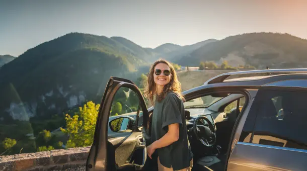 Eine Frau steht an einer geöffneten Autotür und genießt den Ausblick.