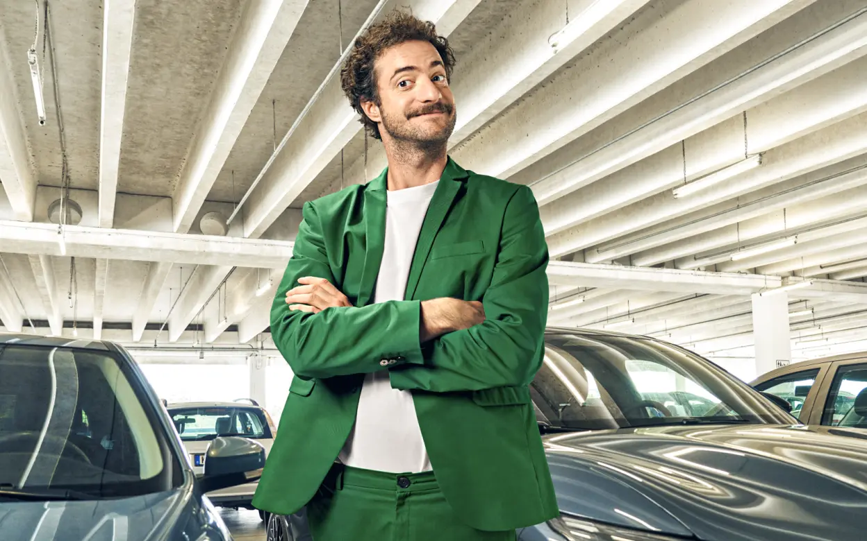 Ein Mann steht schmunzelnd mit verschränkten Armen in einem Parkhaus vor Autos.