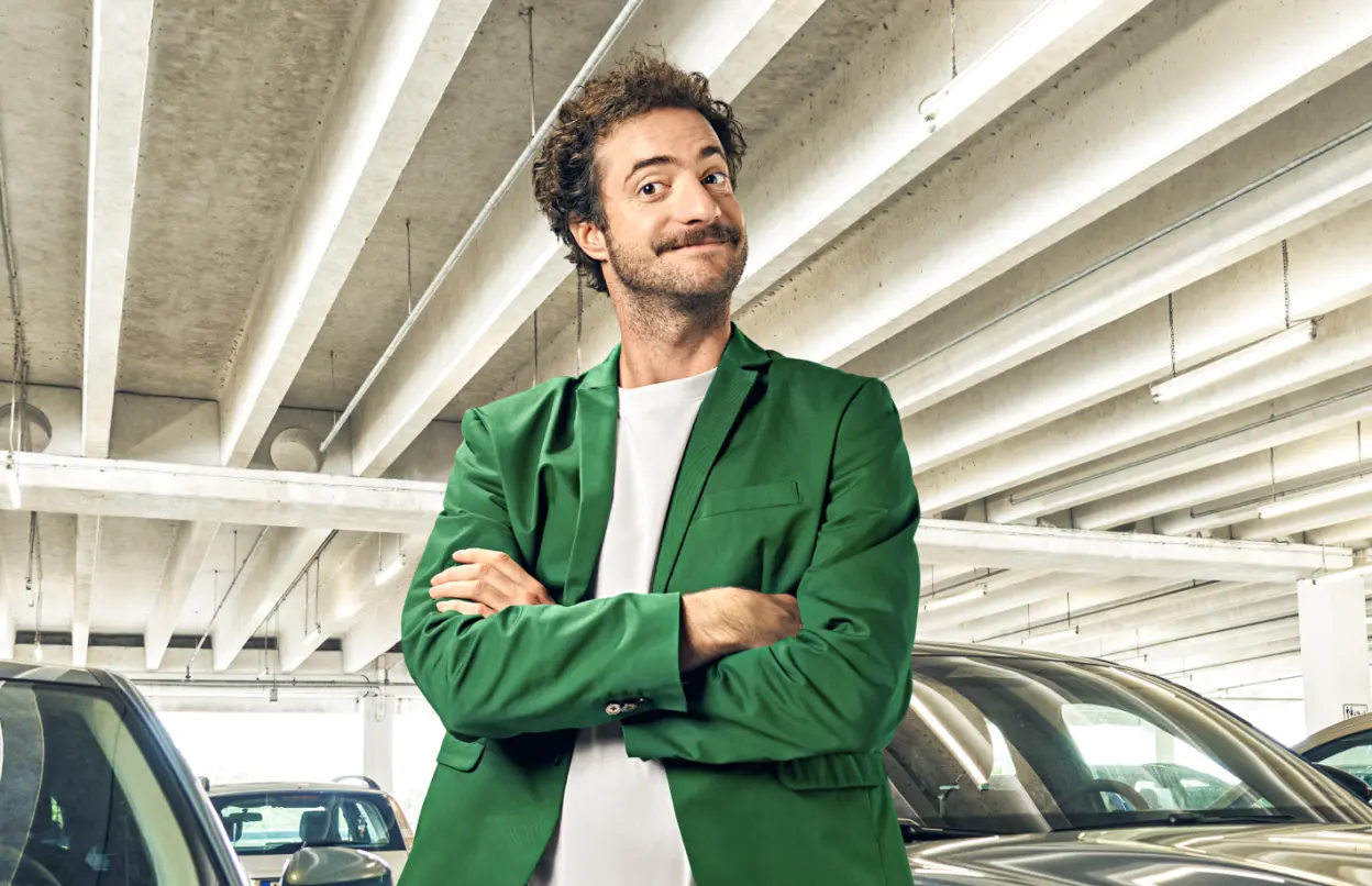 Ein Mann steht schmunzelnd mit verschränkten Armen in einem Parkhaus vor Autos.