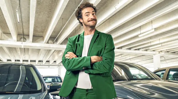 Ein Mann steht schmunzelnd mit verschränkten Armen in einem Parkhaus vor Autos.