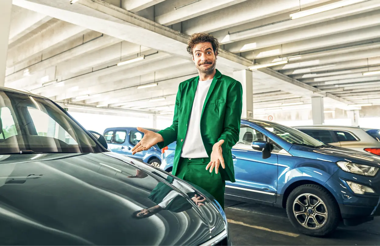 Ein Mann steht im Parkhaus, zieht eine Grimasse und zeigt mit beiden Armen auf ein Auto.