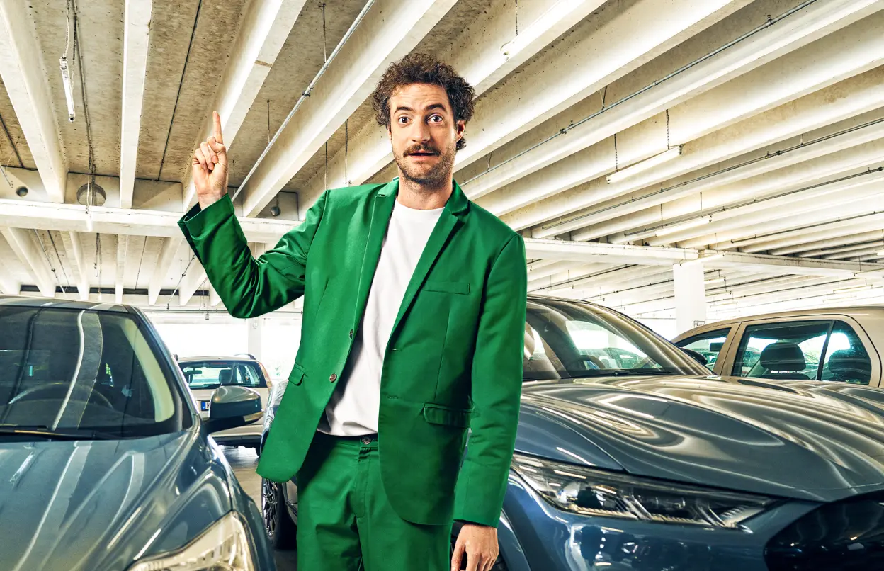 Ein Mann steht in einem Parkhaus und zeigt überrascht nach oben. 