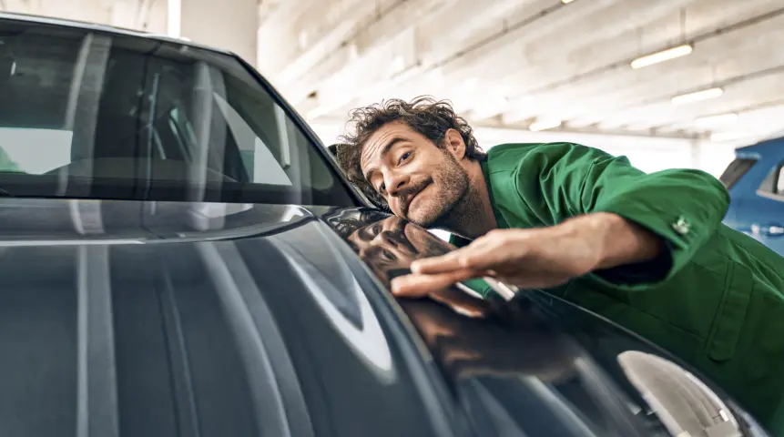 Ein Mann in einem grünen Anzug streicht mit der Hand über die Motorhaube eines Autos.