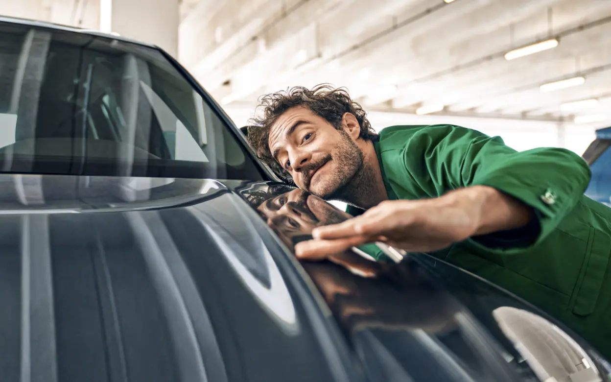 Ein Mann in einem grünen Anzug streicht mit der Hand über die Motorhaube eines Autos.
