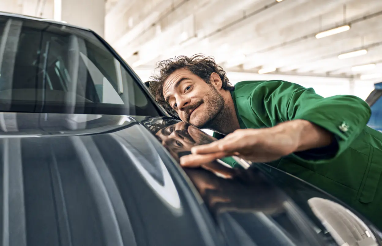Ein Mann in einem grünen Anzug streicht mit der Hand über die Motorhaube eines Autos.