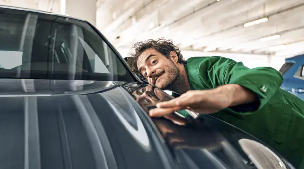 Ein Mann in einem grünen Anzug streicht mit der Hand über die Motorhaube eines Autos.