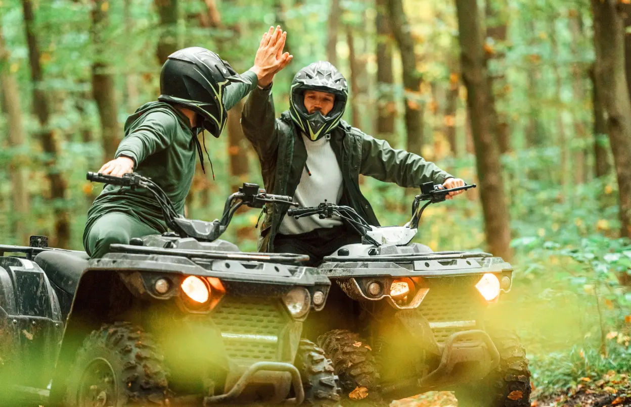Zwei Quadfahrende fahren durch den Wald und geben sich einen Handschlag.