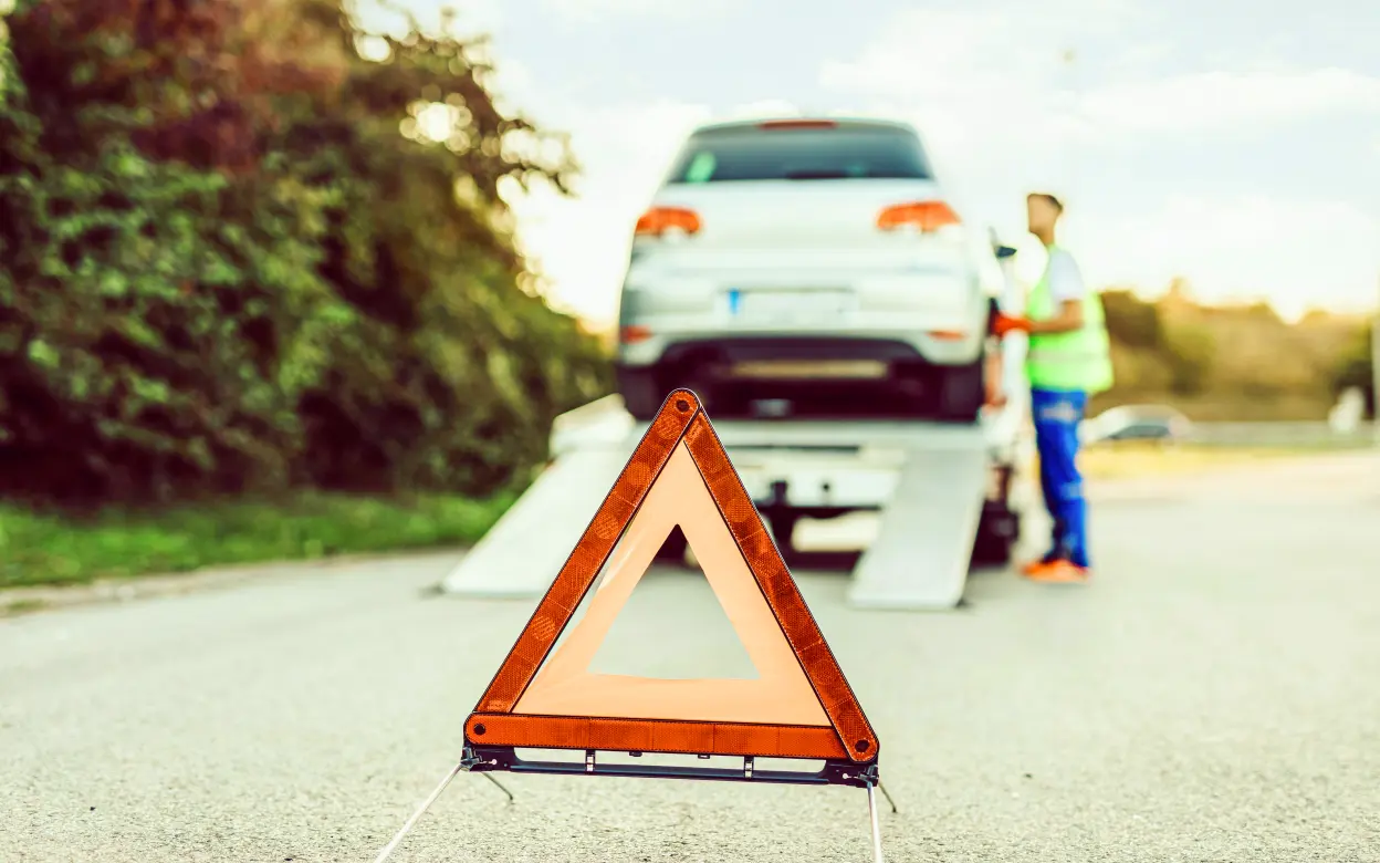 Im Vordergrund ist ein Warndreieck während im Hintergrund ein Auto auf einem Abschleppwagen steht.