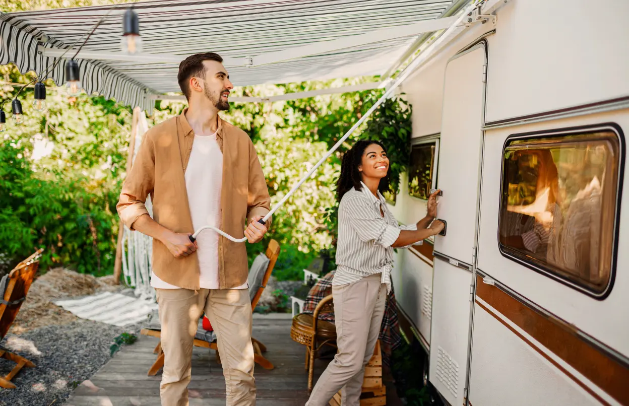 Ein Mann und eine Frau stehen vor einem Wohnwagen und fahren die Markiese aus.