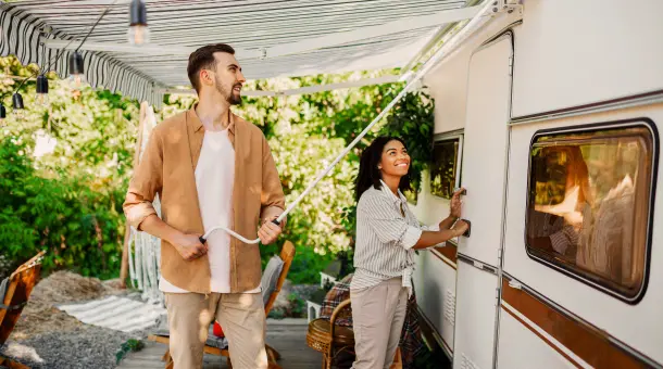 Ein Mann und eine Frau stehen vor einem Wohnwagen und fahren die Markiese aus.