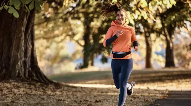 Frau joggt gut gelaunt im herbstlichen Park