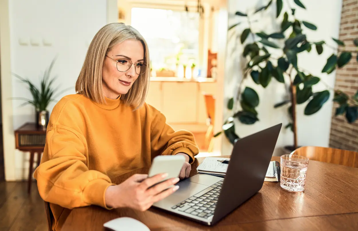Frau sitzt mit Smartphone vor einem Laptop