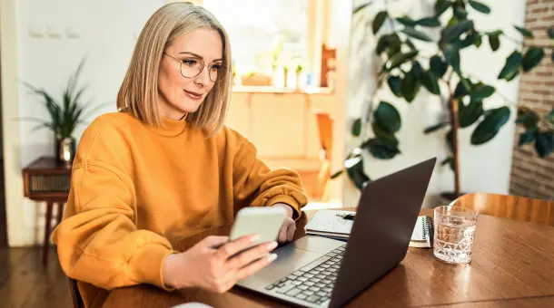 Frau sitzt mit Smartphone vor einem Laptop
