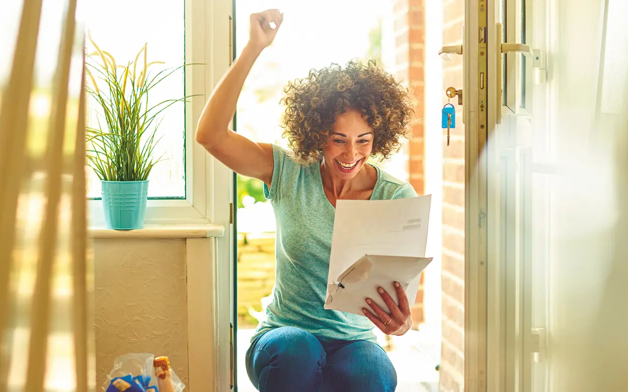 Frau freut sich im Hauseingang über Brief