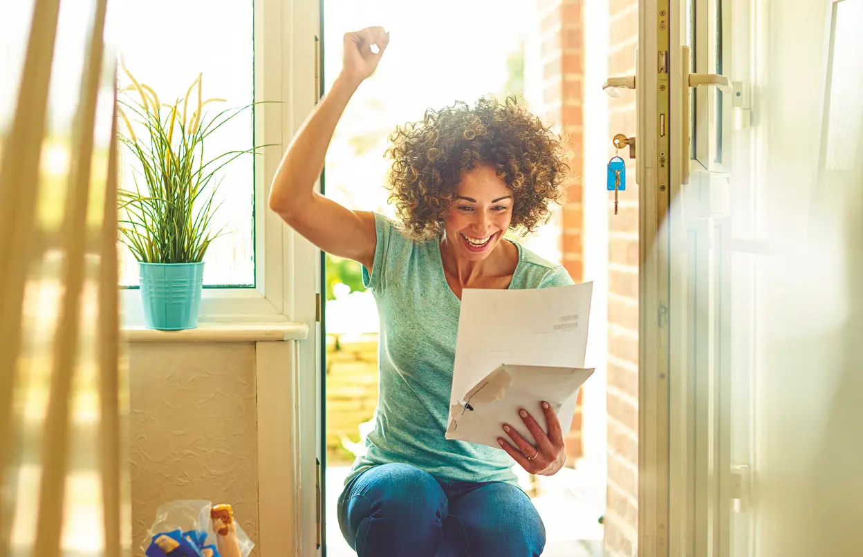 Frau freut sich im Hauseingang über Brief