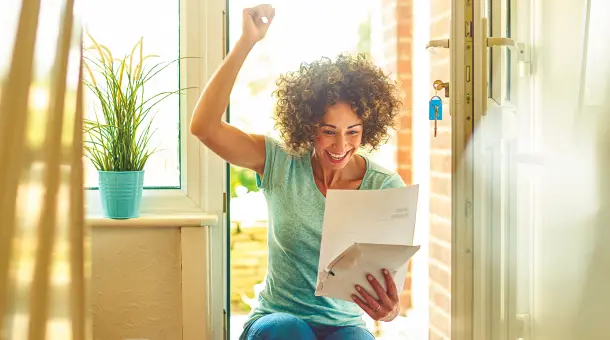 Frau freut sich im Hauseingang über Brief