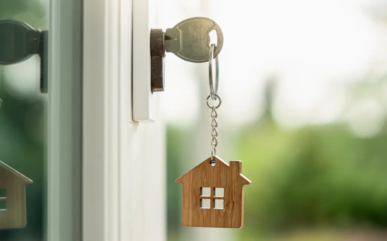 Schlüssel mit Holzhaus-Anhänger steckt in Schloss
