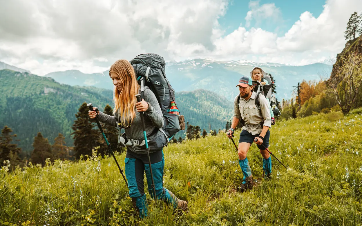 Junges Paar mit kleinem Kind wandert auf grüner Wiese in den Bergen