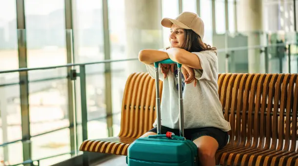 Frau sitzt mit Koffer im Flughafenterminal