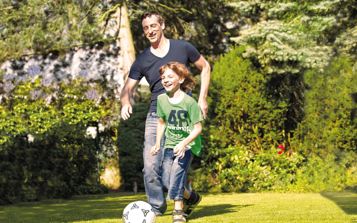 Vater spielt mit Sohn im Garten Fußball