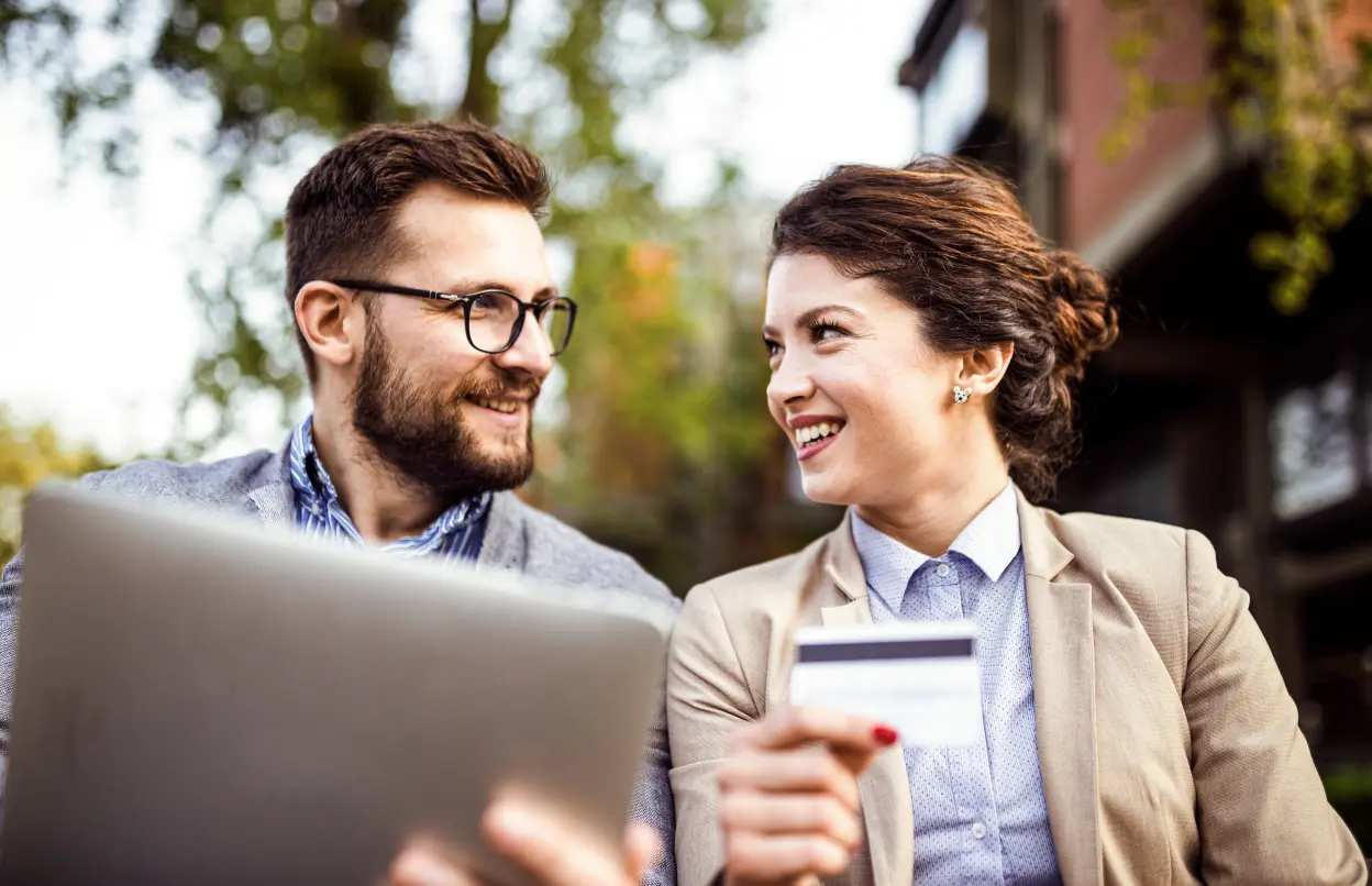 Paar mit Tablet und EC-Karte in den Händen lächelt sich an
