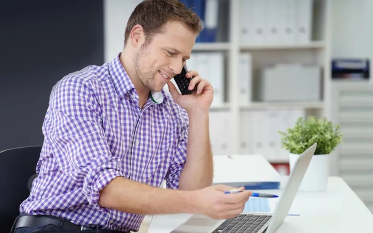 Ein Mann telefoniert und arbeitet dabei an einem Laptop