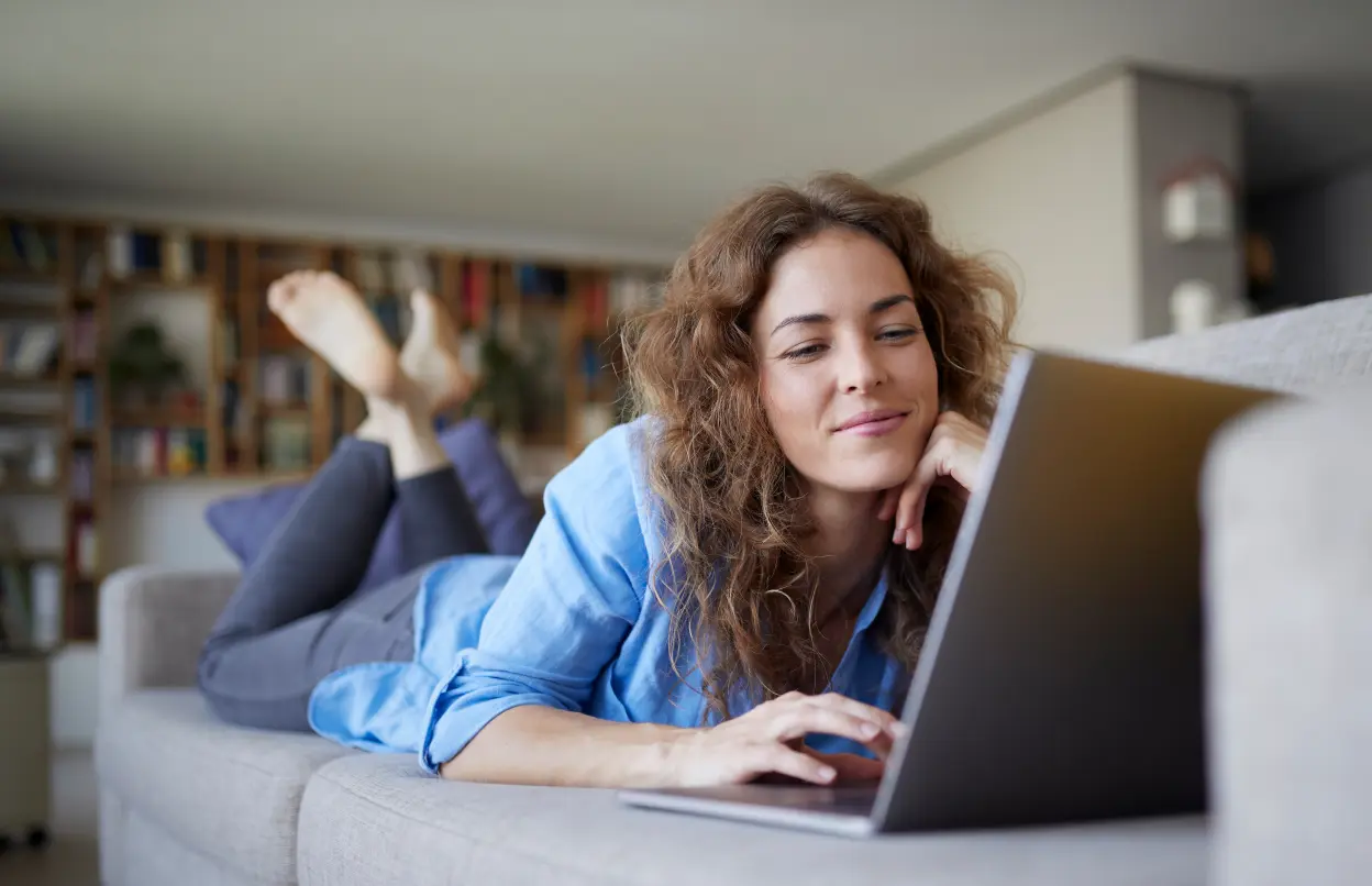 Frau liegt auf Sofa und nutzt ein Laptop