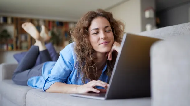 Frau liegt auf Sofa und nutzt ein Laptop