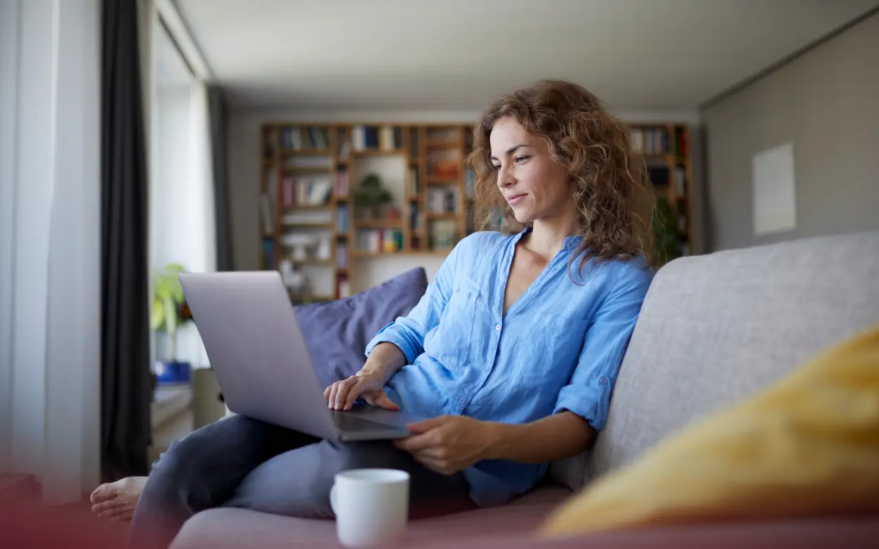 Frau sitzt auf Sofa und nutzt ein Laptop