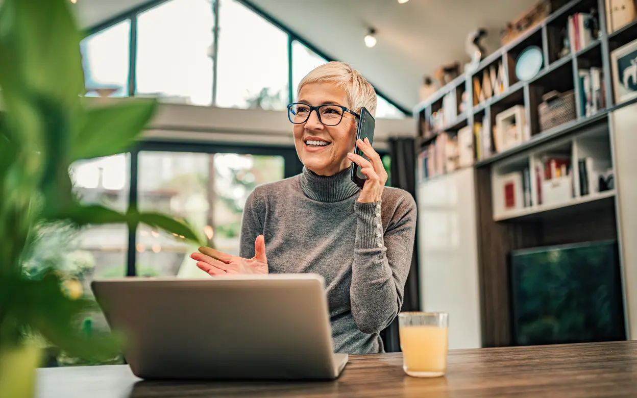 Eine Frau sitzt lächelnd vor ihrem Laptop und telefoniert.