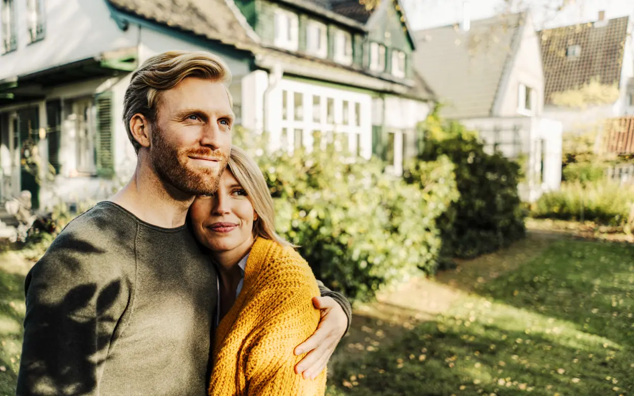 Eine Frau und ein Mann umarmen sich vor einem Haus.