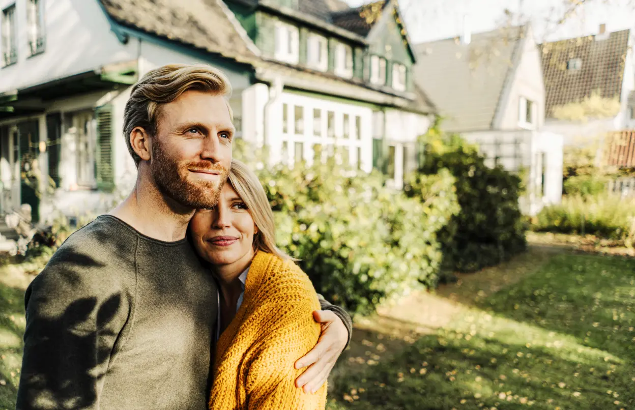 Eine Frau und ein Mann umarmen sich vor einem Haus.