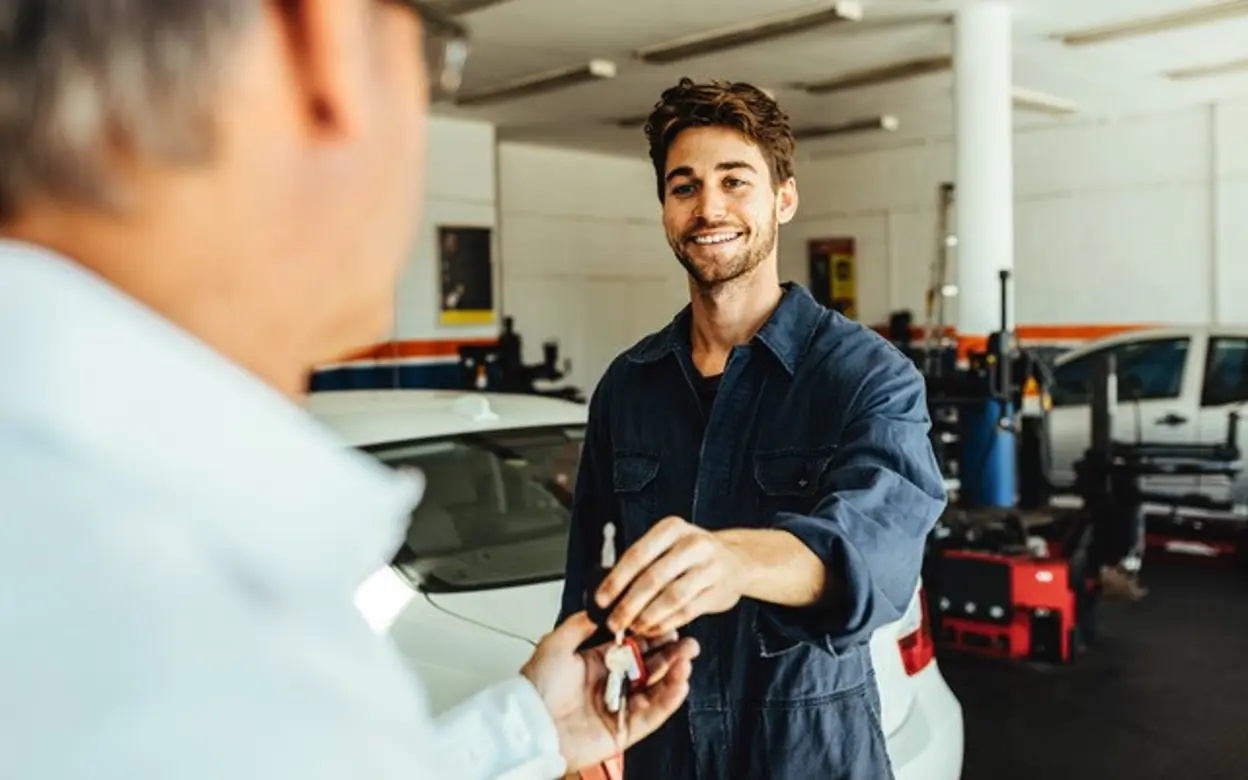 Ein Mitarbeiter überreicht einem Kunden in einer Autowerkstatt einen Autoschlüssel.
