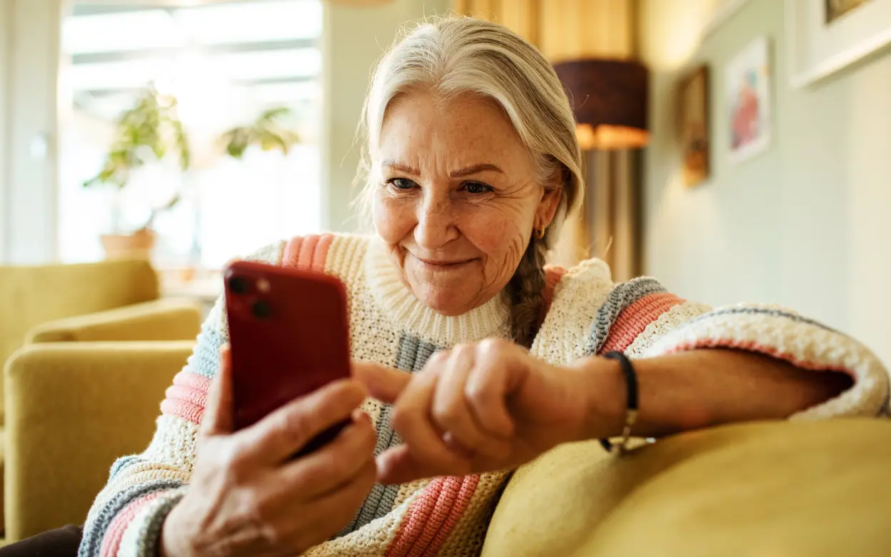 Eine Frau schaut lächelnd auf ihr Handy.