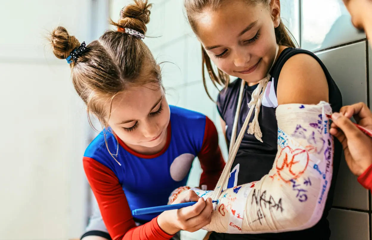 Ein Kind trägt einen Gips am Arm auf dem andere Kinder unterschreiben.