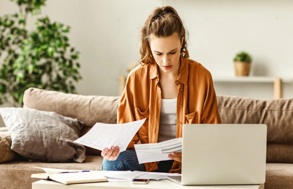 Besorgte Frau liest Unterlagen vor ihrem Laptop