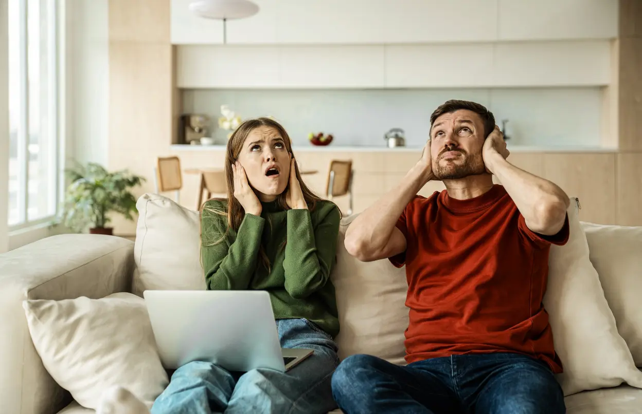 Mann und Frau sitzen auf dem Sofa und halten sich die Ohren zu 