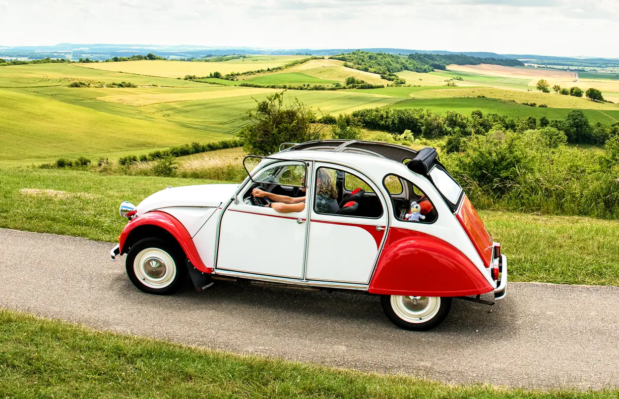 Citroën 2CV fährt durch grüne Landschaft