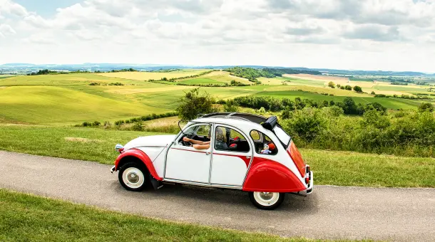Citroën 2CV fährt durch grüne Landschaft