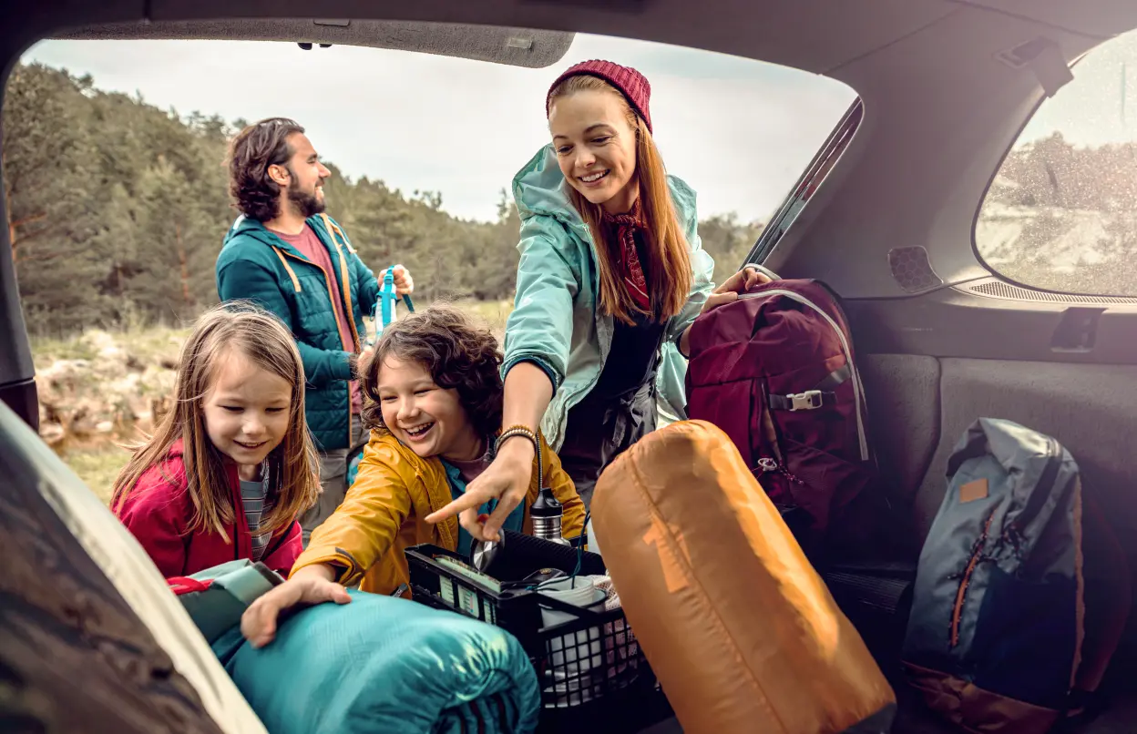 Familie entlädt Campingsachen aus dem Kofferraum 