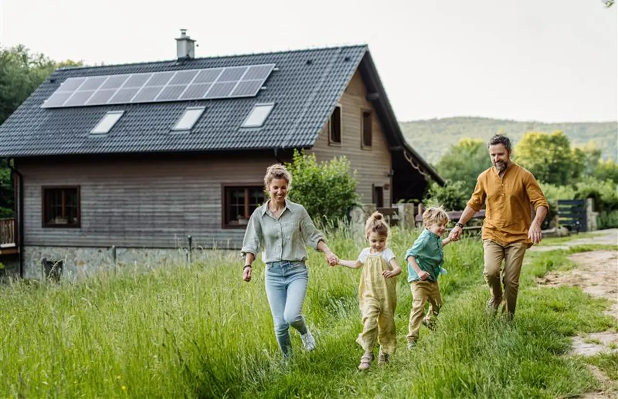 Eine glückliche Familie vor einem Haus mit Photovoltaikanlage auf dem Dach