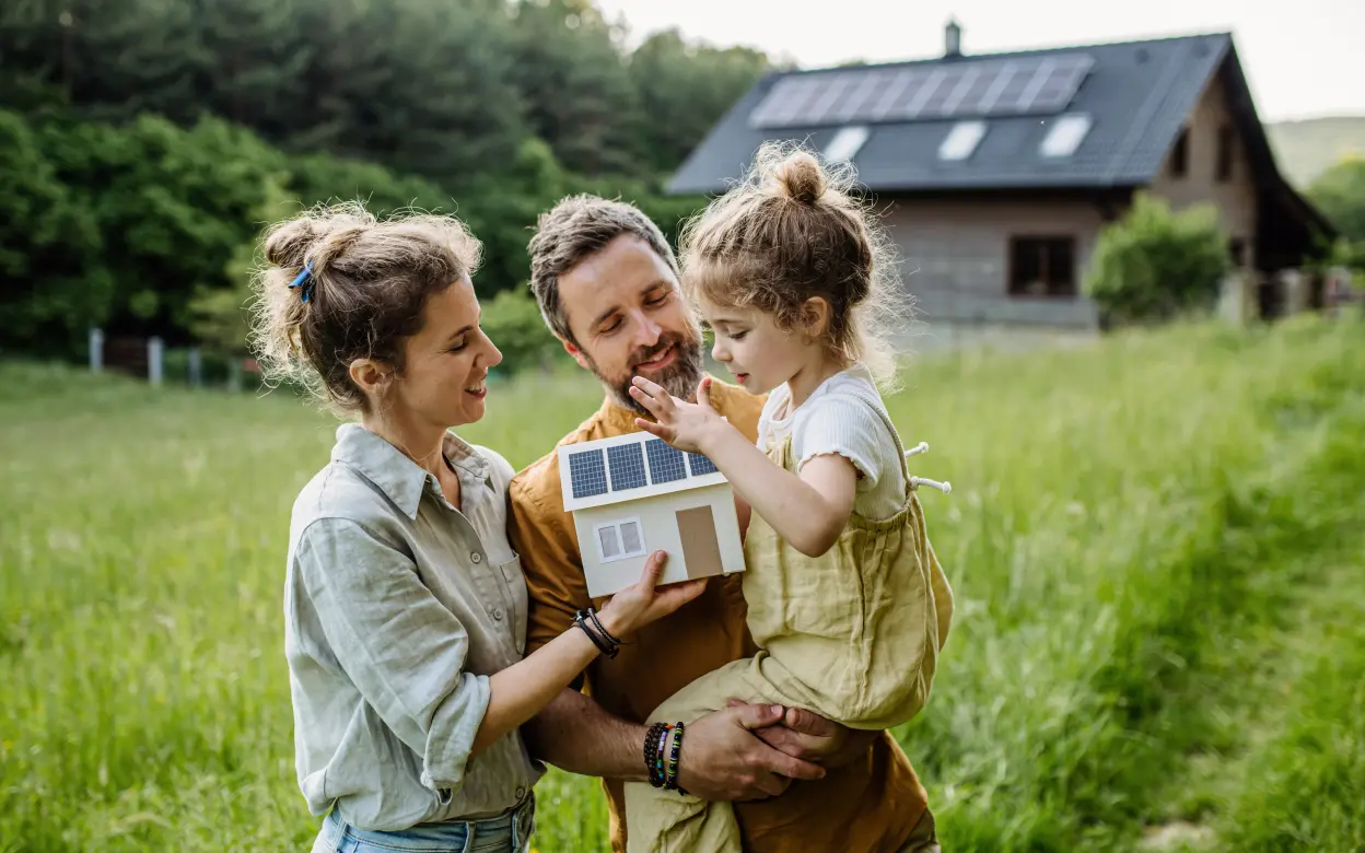 Eine Familie mit einem kleinen Spielhaus vor einem Haus mit PV-Anlage auf dem Dach