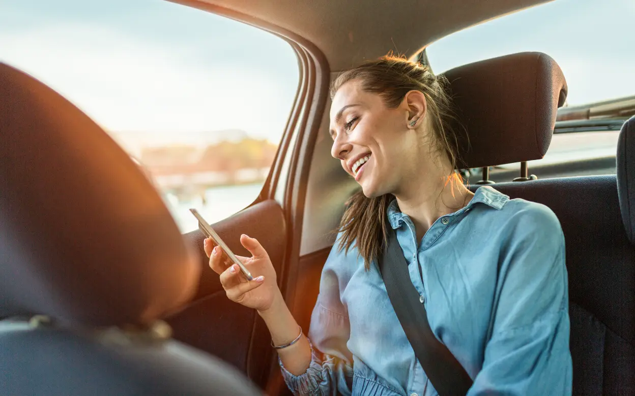Frau sitzt mit Smarthphone auf Autorücksitz