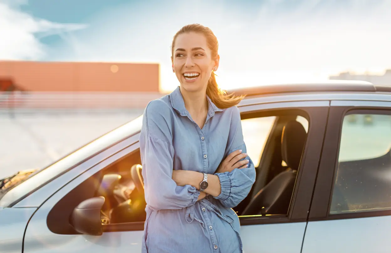 Frau steht lächelnd an Autotür