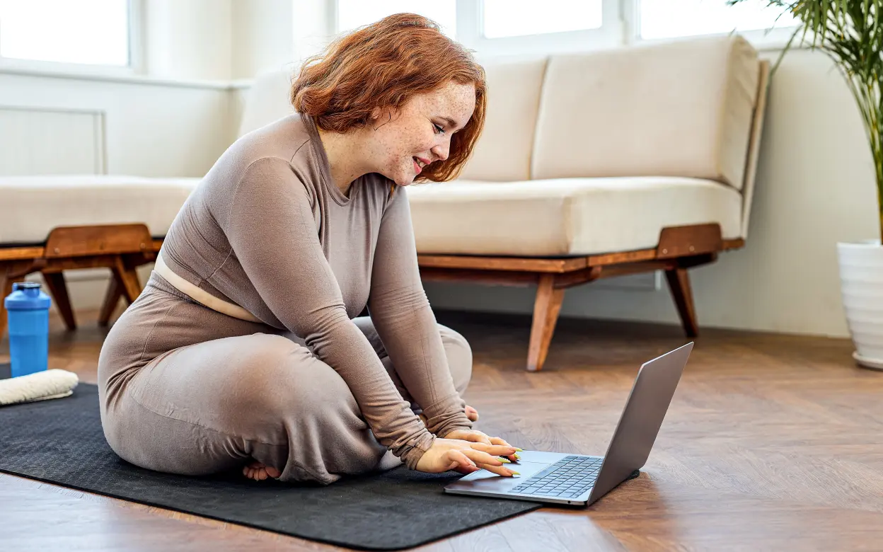 Frau sitzt mit Yogamatte auf Laptop