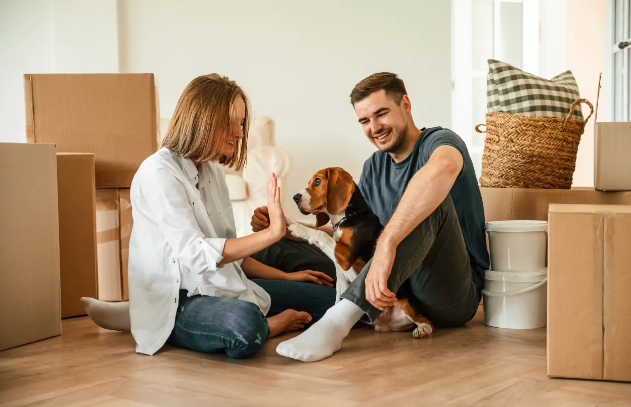 Paar sitzt mit Hund auf dem Fußboden in neuer Wohnung