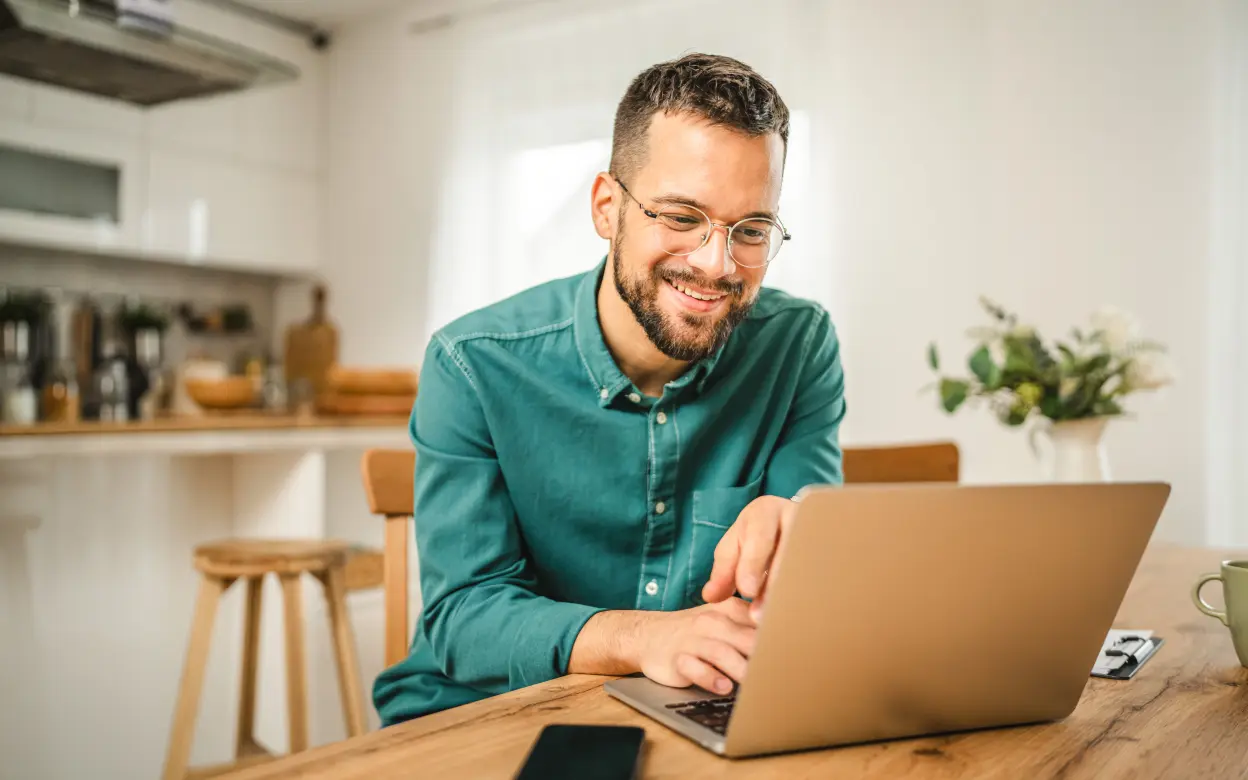 Mann sitzt in Küche vor Laptop